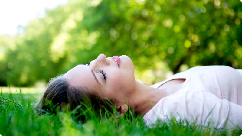 Estresse como Aliviar: 10 Técnicas Simples de Relaxamento. Mulher relaxada desfrutando de técnicas de relaxamento para aliviar o estresse, deitada na grama ao ar livre