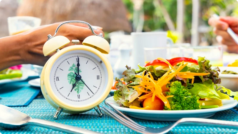 Legumes frescos em destaque ao lado de um relógio despertador antigo, simbolizando o início de uma jornada saudável com o Jejum Intermitente.