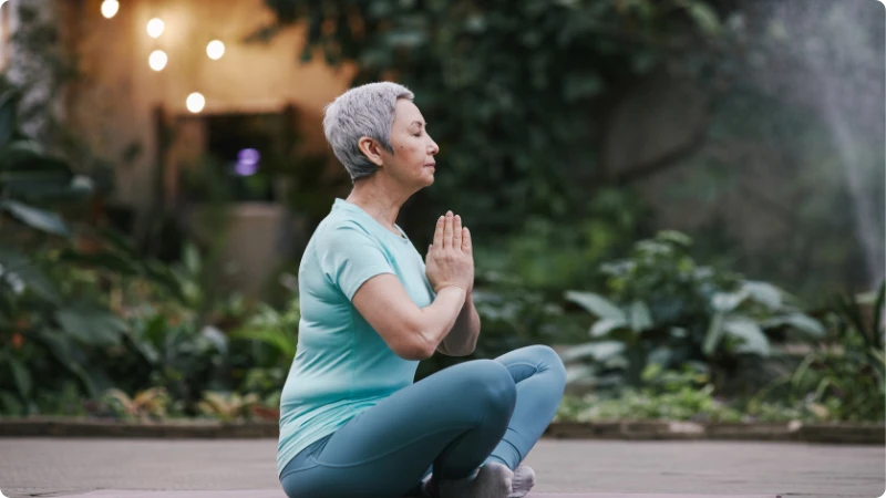 Mulher idosa praticando meditação ao ar livre para aliviar a dor crônica no envelhecimento.