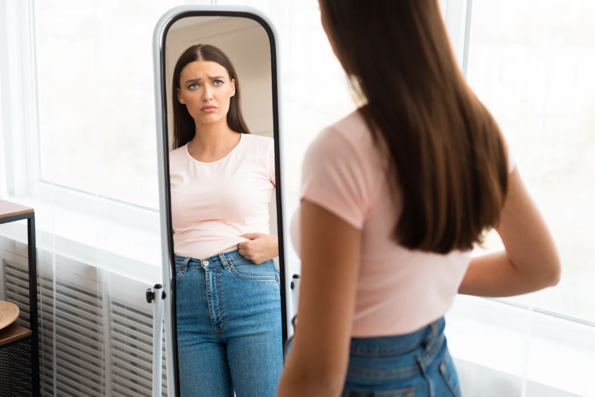 Imagem Corporal: O Que É e Como Ter uma Relação Saudável. Uma mulher se olhando no espelho demonstrando insatisfação com o seu corpo.