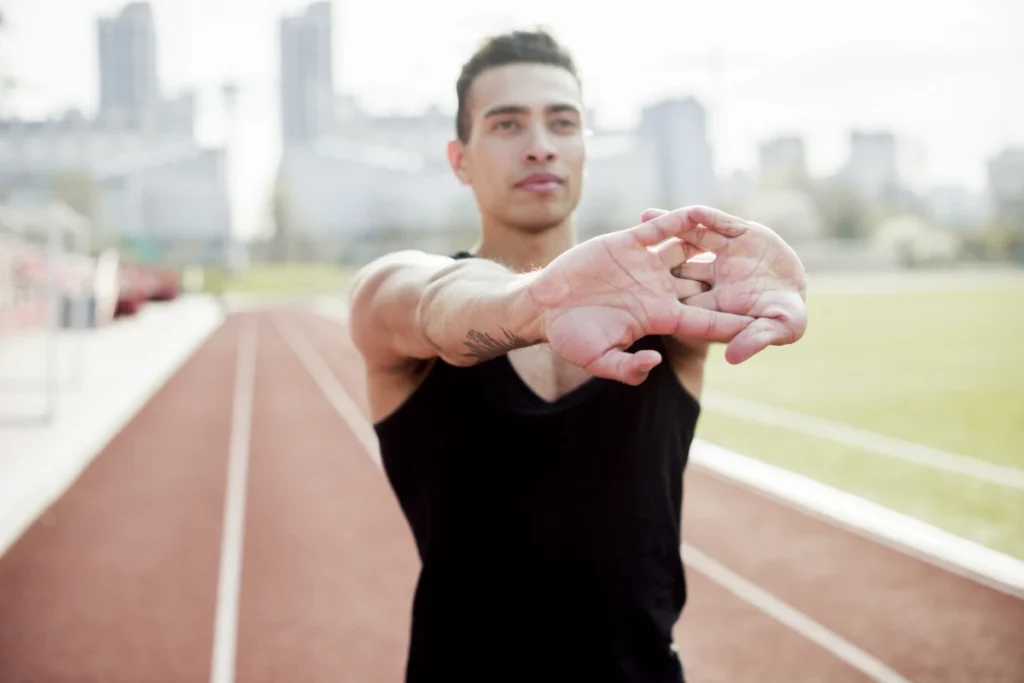 7 Benefícios do Alongamento: Seu Corpo Vai Agradecer. Imagem de um atleta sexo masculino esticando as mãos antes de correr na pista de corrida.