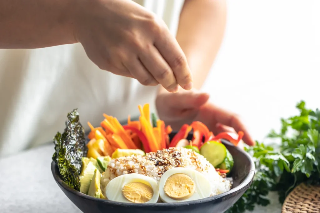 Dieta Low Carb: o que é, como fazer, benefícios e cardápio. Uma pessoa preparando uma refeição em uma tigela caseira com legumes de arroz e ovos.