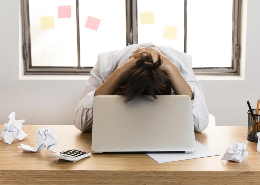 Motivação: o que é, tipos e como desenvolver na vida. Um rapaz jovem sentado em uma mesa de escritório de cabeça baixa desmotivado no trabalho.