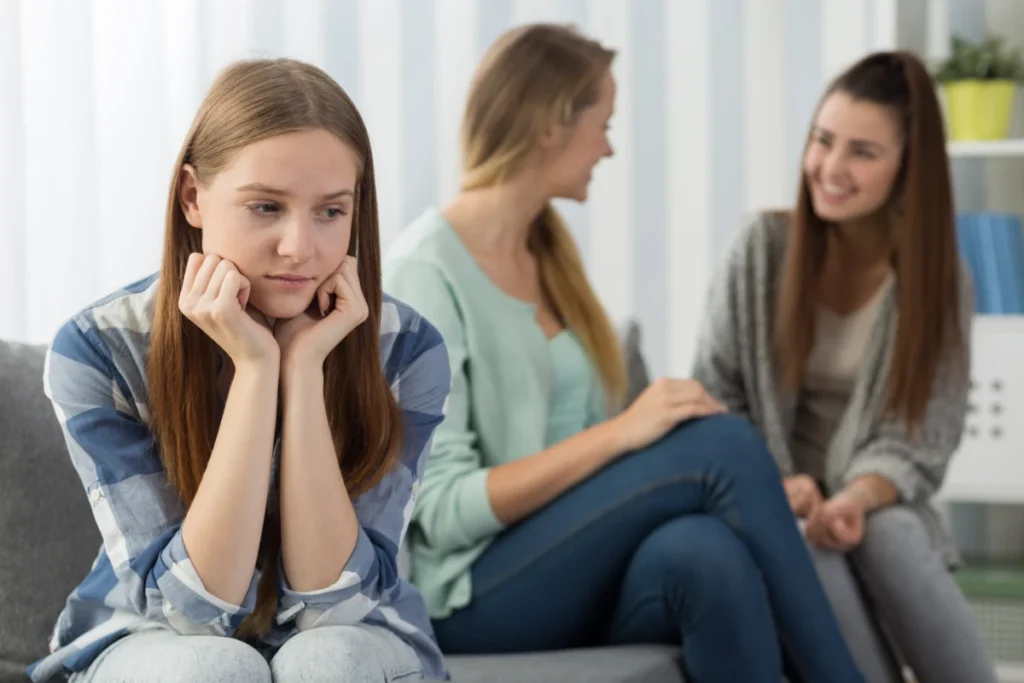 Ansiedade: O que é, causas, sintomas e tratamento. Garota jovem sentada na sala separada de outras pessoas, fobia social