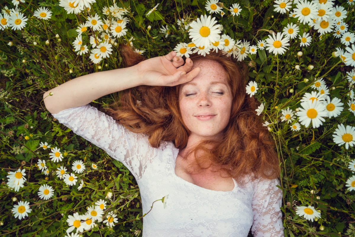 Camomila: o que é, para que serve, benefícios e como usar. Mulher deitada no campo de camomila.