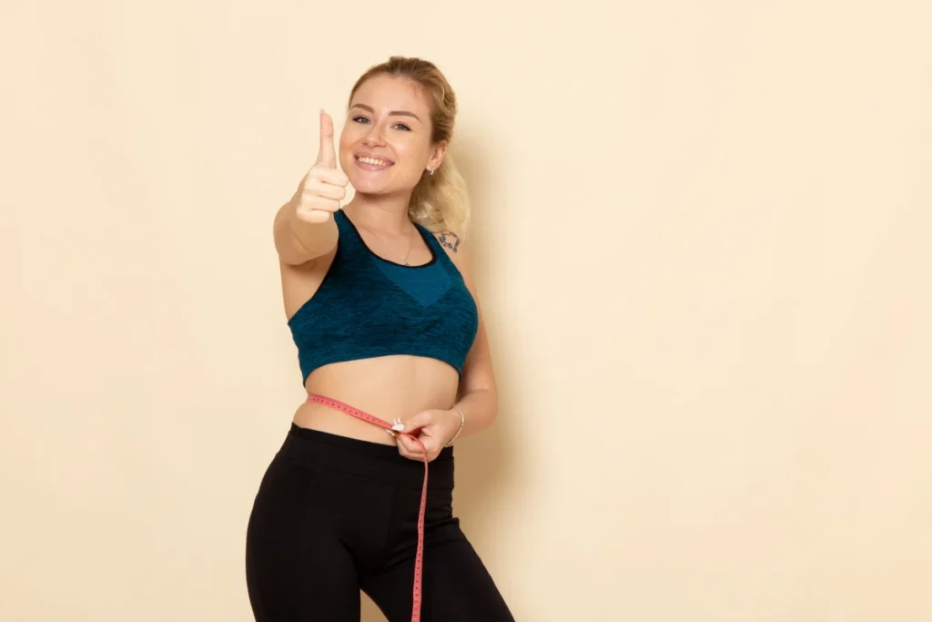 Cardápio para Emagrecer: Plano de 5 Dias Completo. Jovem mulher com roupa esportiva medindo o corpo com um sorriso.