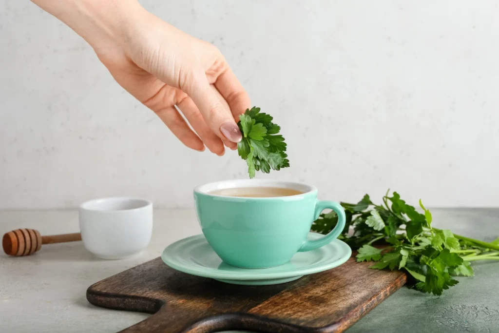 Chá de Salsa Emagrece? 7 Benefícios e Como Preparar. Mulher preparando chá quente com salsa em fundo claro.
