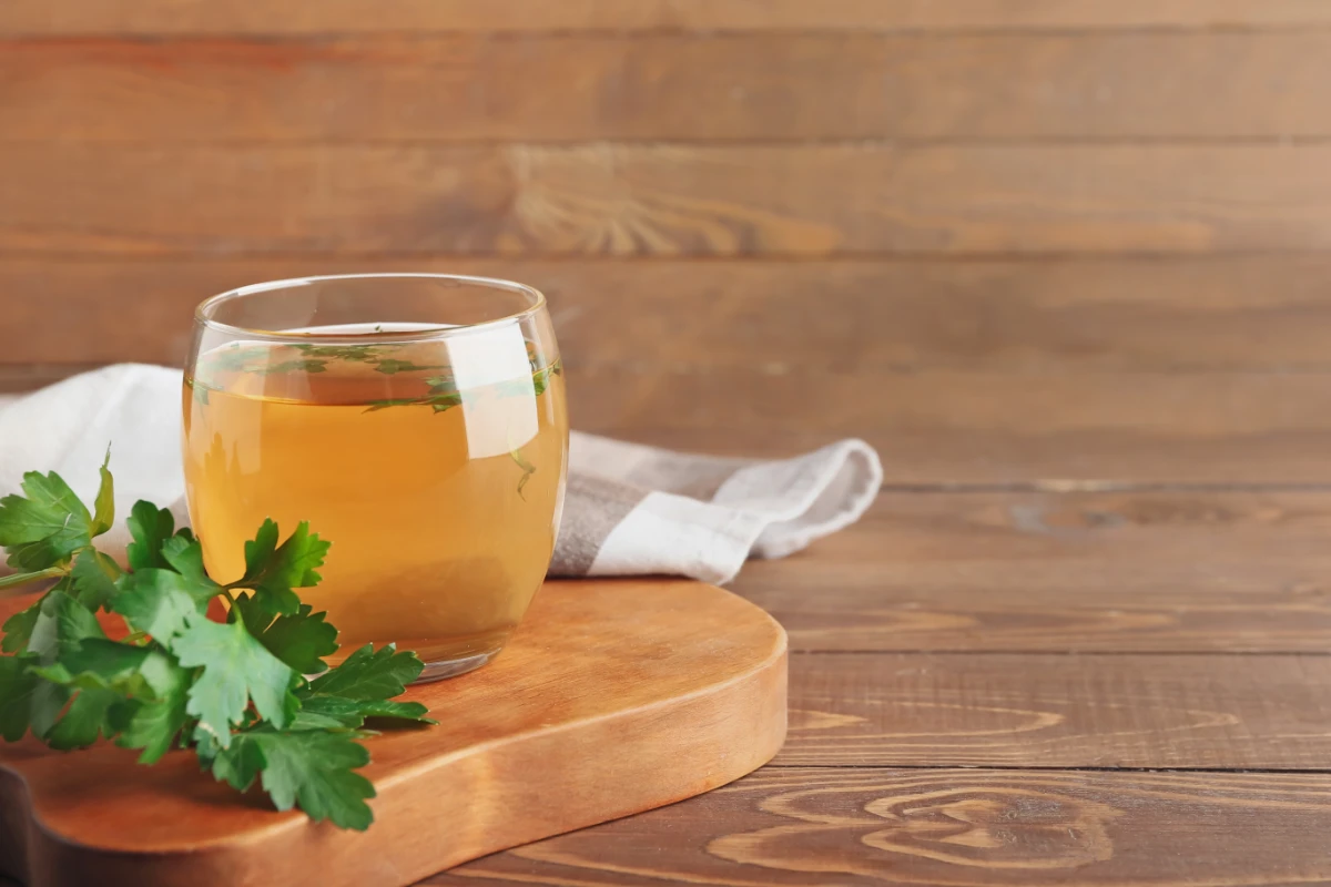 Chá de Salsa Emagrece? 7 Benefícios e Como Preparar. Xícara de chá quente e salsa em fundo de madeira.