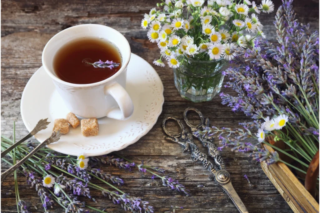 Chás para Dormir: 7 Melhores Opções Naturais e Como Fazer 3. Sobre a mesa uma xícara de chá de lavanda e camomila, com lavanda fresca e camomila selvagem, com uma tesoura e talheres em estilo rústico.