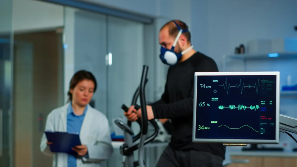 Como Descobrir Sua Frequência Cardíaca para Emagrecer. Equipe de médicos monitorando na tela computador no laboratório a frequência cardíaca e resistência de paciente masculino fazendo atividade física.
