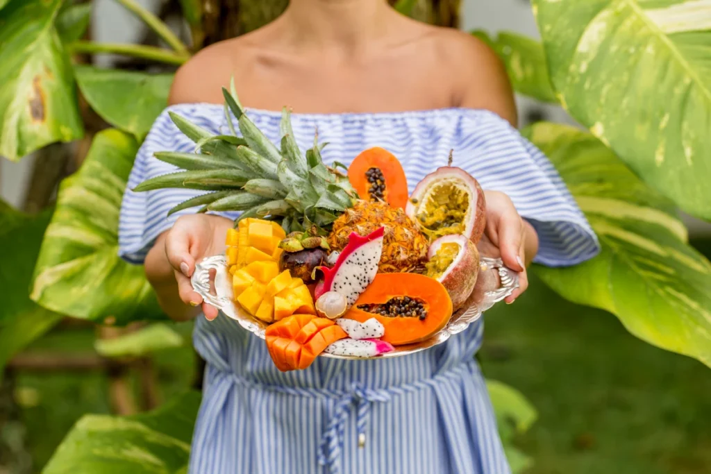 Dieta Mediterrânea: O Que é, Benefícios e Como Fazer. Mulher oferecendo frutas tropicais brasileiras em uma bandeja.
