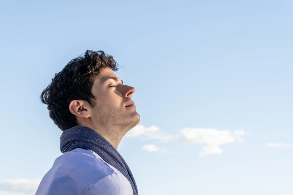 Doenças Respiratórias no Inverno Como Prevenir. Homem jovem de cachecol, com a cabeça para o céu e os olhos fechados respirando ar puro de qualidade.