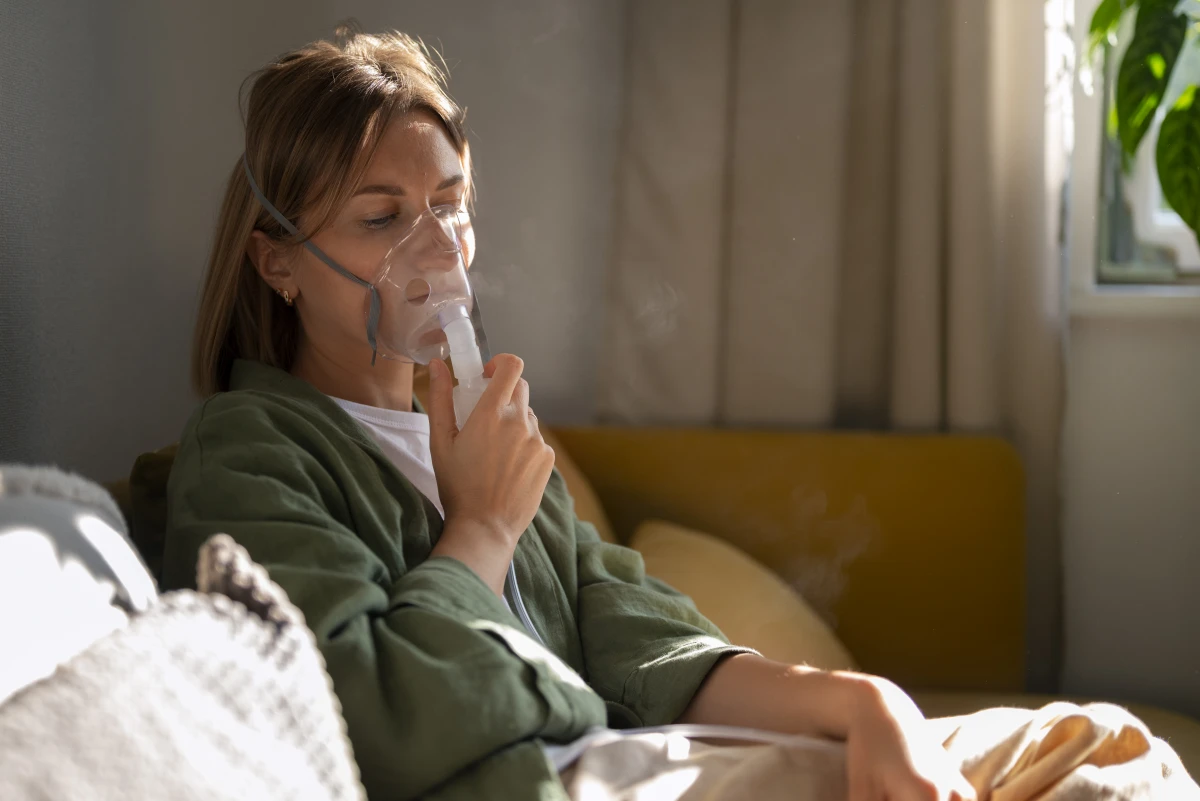 Doenças Respiratórias no Inverno Como Prevenir. Mulher de vista lateral sentada no sofá da sala, tendo crise respiratória usando nebulizador.