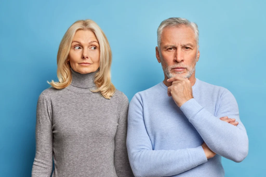 Longevidade: 8 Pilares para uma Vida Longa e Plena. Homem e mulher madura sérios, estão próximos um do outro com expressões atenciosas vestidos com roupas casuais isoladas sobre parede azul.