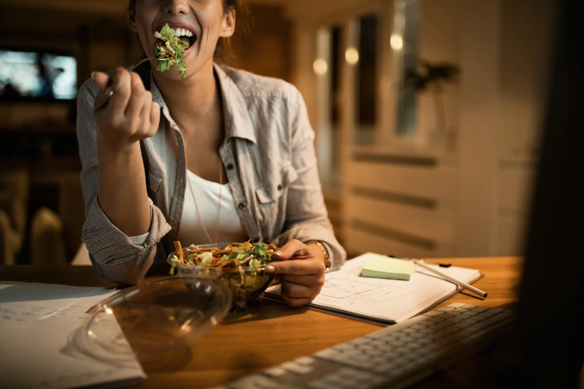 O Que Comer à Noite Para Não Engordar. Mulher jovem usando computador e comendo salada a noite em casa.