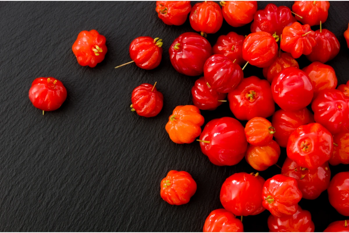 Pitanga: O que é, Benefícios, Tipos e Como Consumir. Várias pitangas maduras sobre um fundo preto.