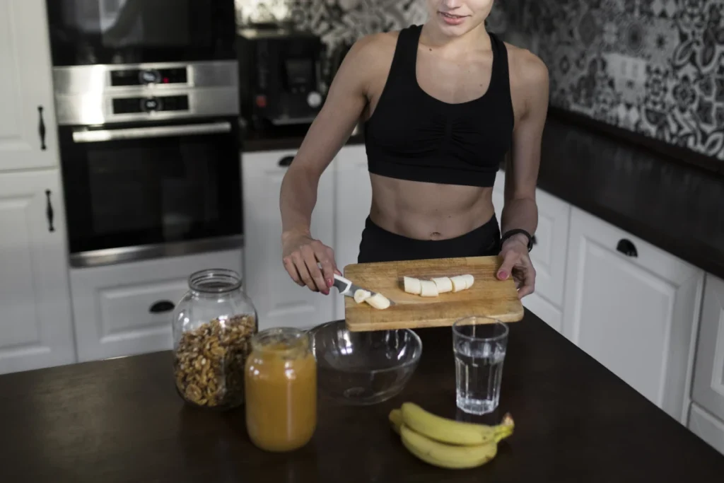 Proteínas: O Que São, Funções e Como Incluir na Dieta. Mulher na cozinha de corpo atlético, com roupa esportiva, preparando uma refeição saudável rica em proteínas.