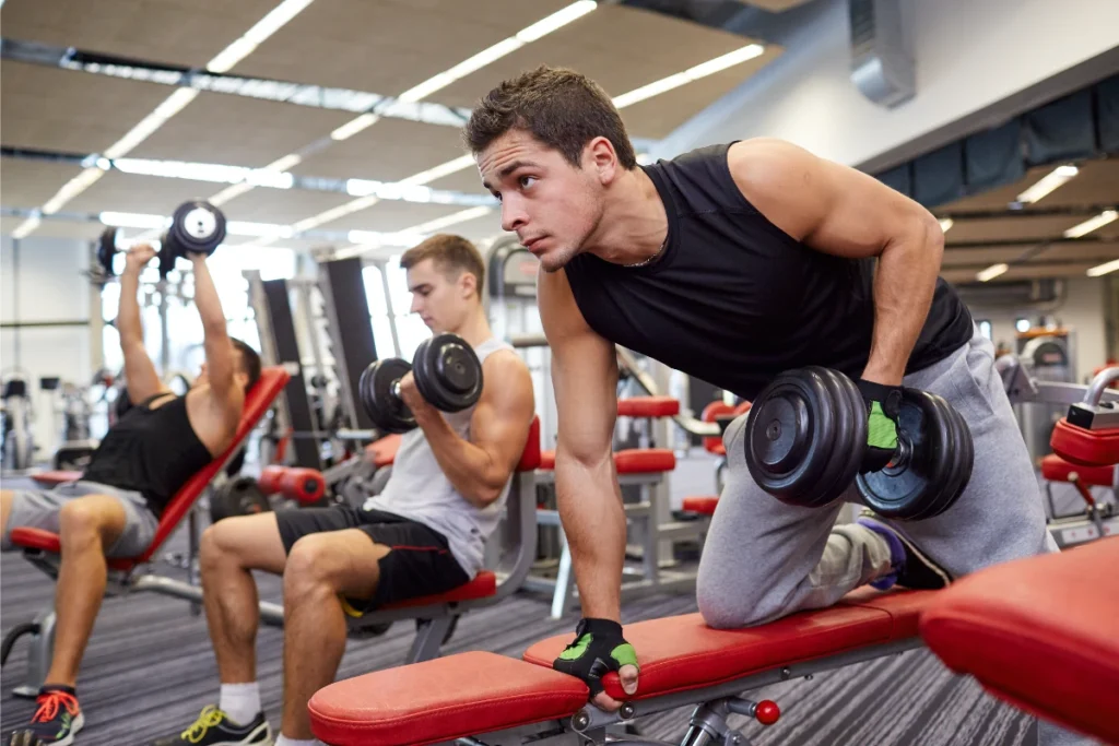 Treino ABC: O Que É, Como Fazer, Benefícios e Cronogramas. Homens jovens fazendo vários exercícios com halteres na academia.