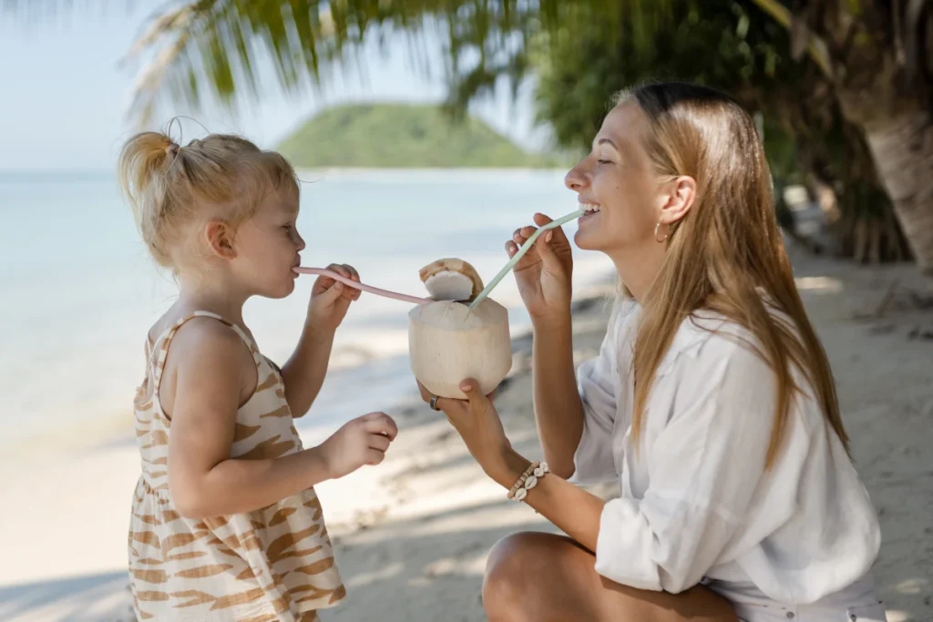 Água de Coco: benefícios, propriedades e como consumir. Mãe e filha curtindo suas férias ensolaradas tomando água de coco.