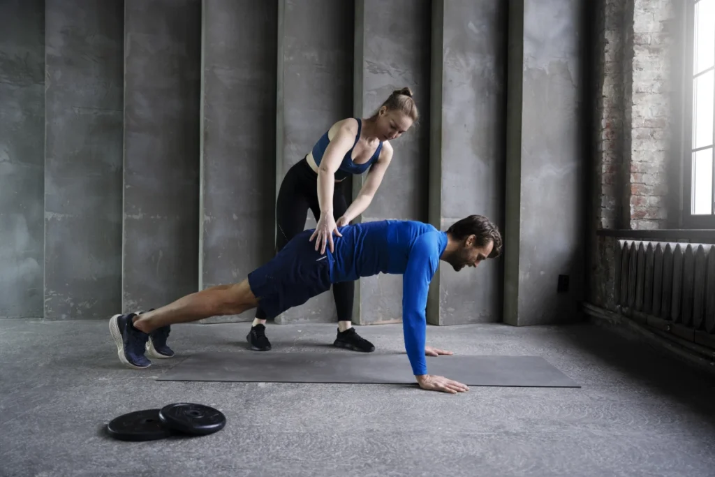 Burpee: o que é, benefícios e como fazer corretamente. Mulher de jovem corrigindo o homem nos exercícios de burpee.