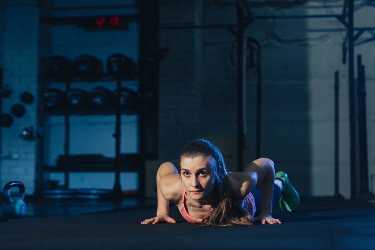 Burpee: o que é, benefícios e como fazer corretamente. Mulher em forma, com roupa esportiva colorida, fazendo burpee em colchonete em uma academia.