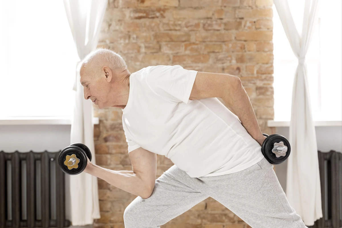 Homem sênior realizando exercícios de musculação para idosos segurando halteres em posição de treino