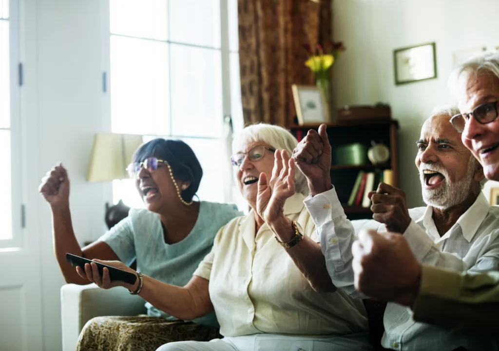 Atividades para idosos: 50+ opções práticas e seguras. Grupo de idosos assistindo televisão juntos.