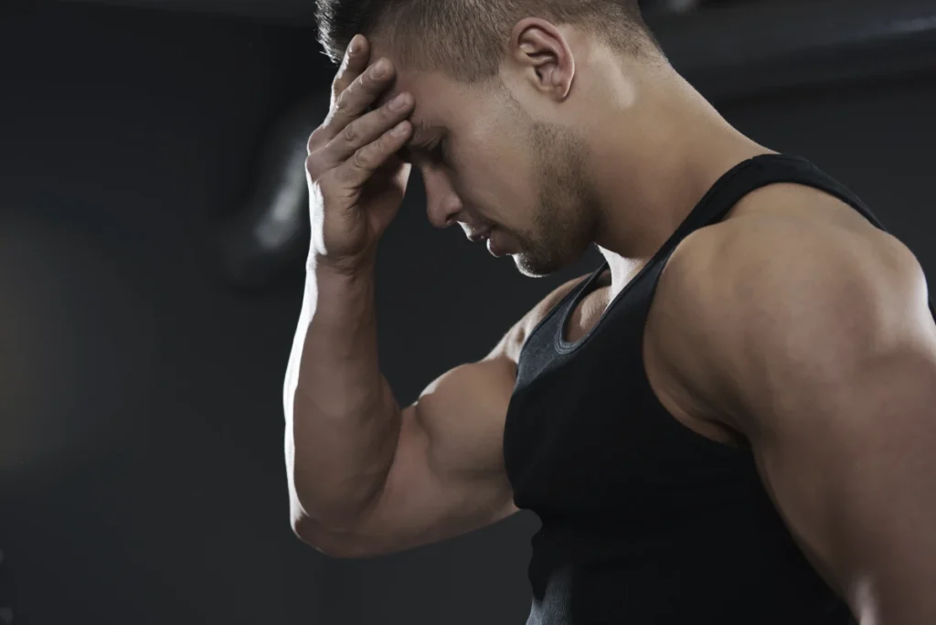 Homem jovem forte na academia de musculação pensativo com a mão direita na cabeça.