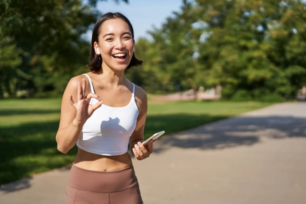 Mulher jovem desportista asiática feliz mostrando sinais de aprovação a exercícios sorridentes depois de uma caminhada em um parque dizendo que sim aprova.