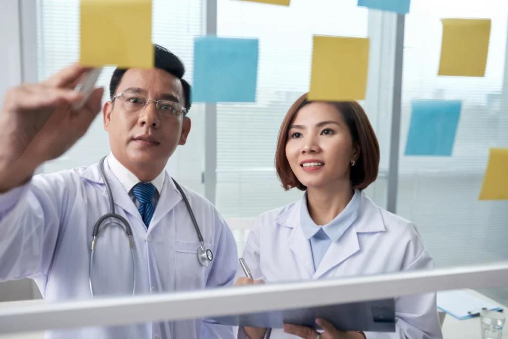 Dois colegas médicos asiáticos revisando os adesivos de memória no painel de vidro.