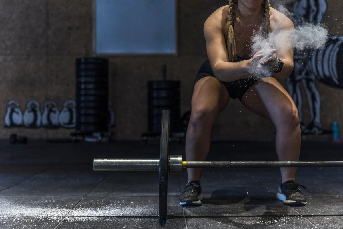 Mulher atlética com magnésio nas mãos se preparando para treino de força em academia