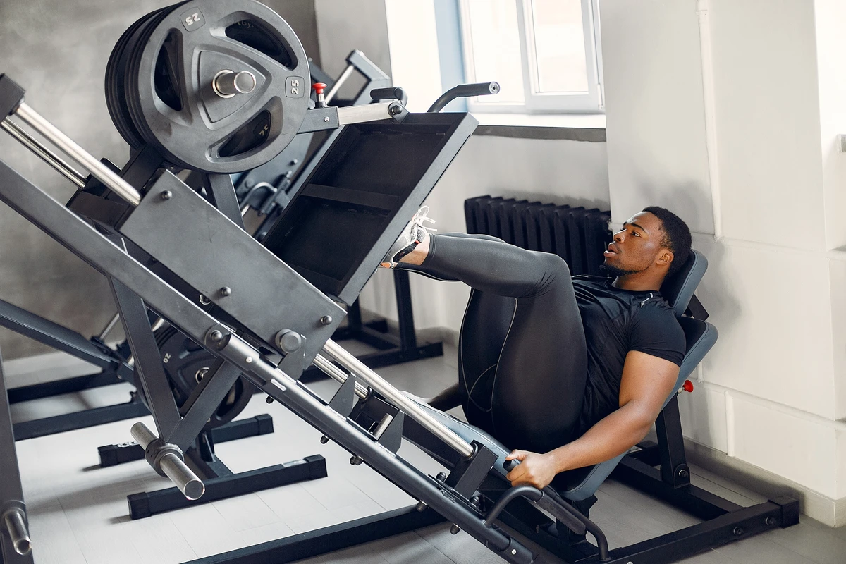 Homem negro realizando treino de força em ginásio, demonstrando exercícios de musculação com equipamentos