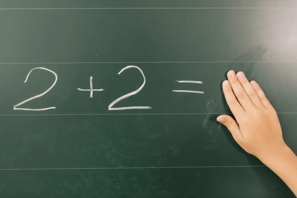 Como Calcular Sua Frequência Cardíaca Máxima. Mão de aluno apagando números em um quadro negro na aula de matemática.