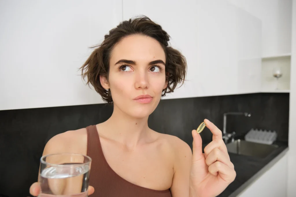 Mulher atlética segurando suplementos vitamínicos enquanto questiona se suplementação de colágeno funciona mesmo